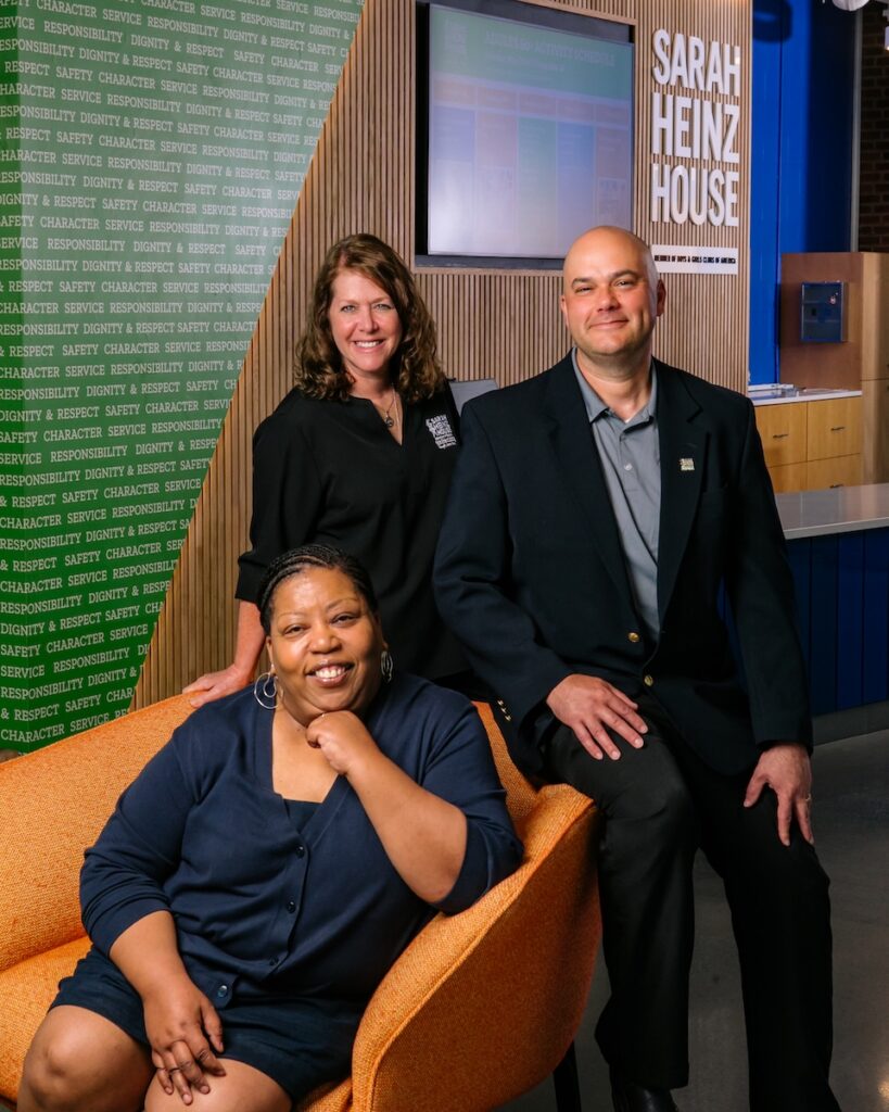 Three leaders of Sarah Heinz House with one woman sitting in an orange chair and another woman and man standing behind the chair.