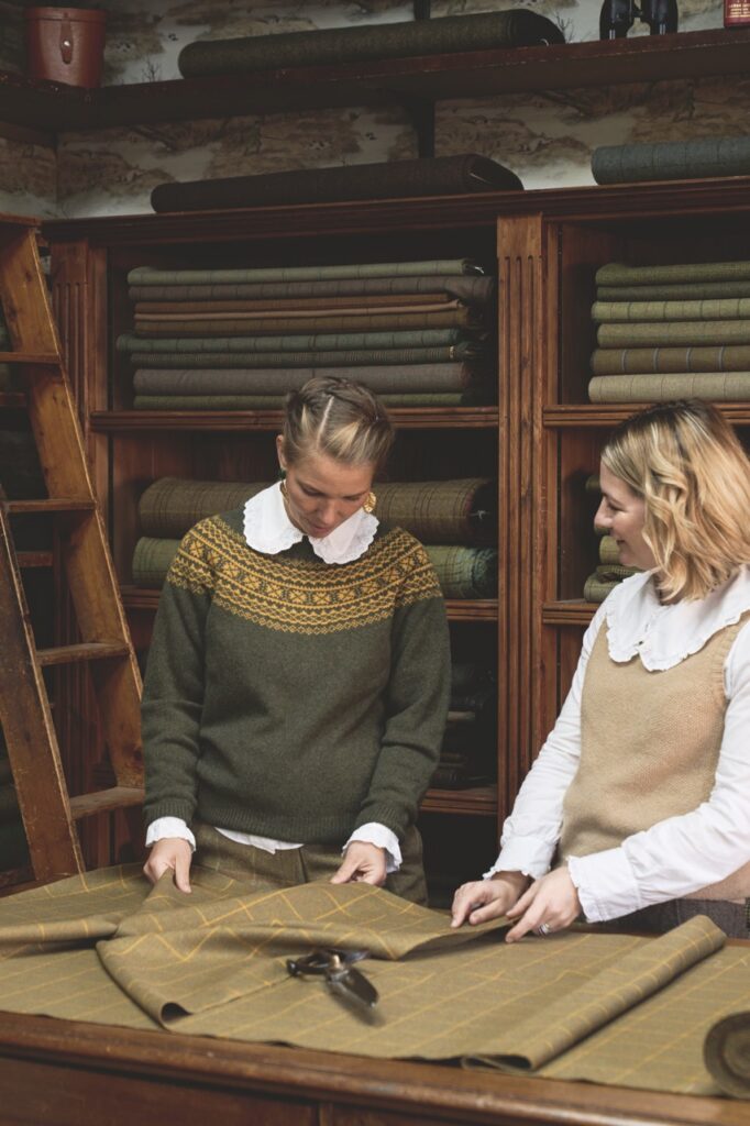 Two women looking at tweed fabric on a table.