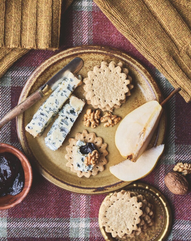 A plaid table cloth with a brown plate, crackers and blue cheese on top.