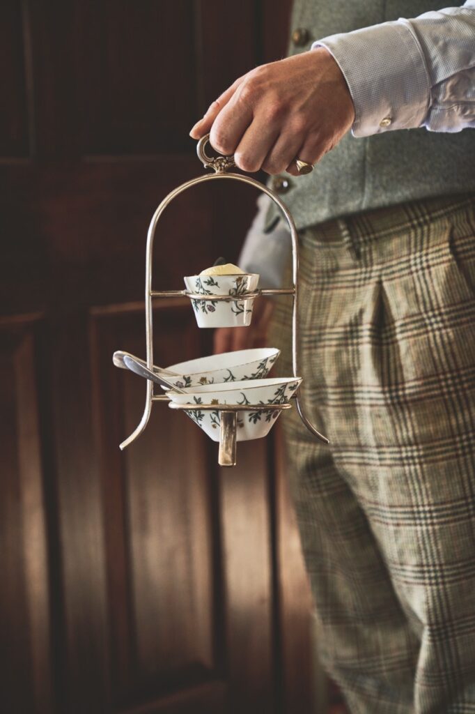 A man in fancy clothing holding a rack of tea and pastries.