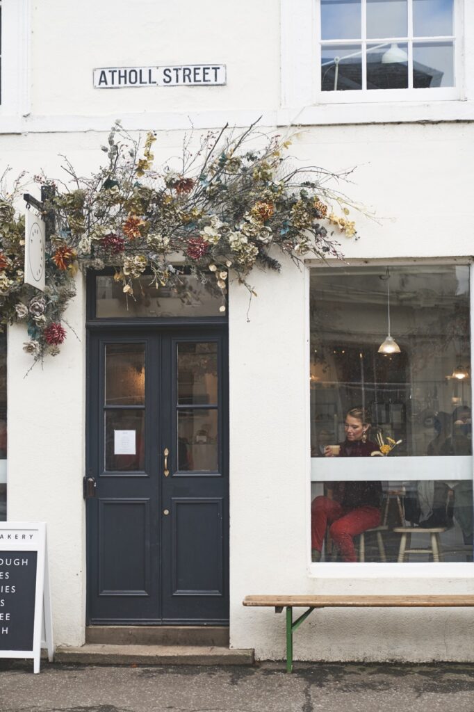 The outside of a Scottish storefront in white and flowers above the door.