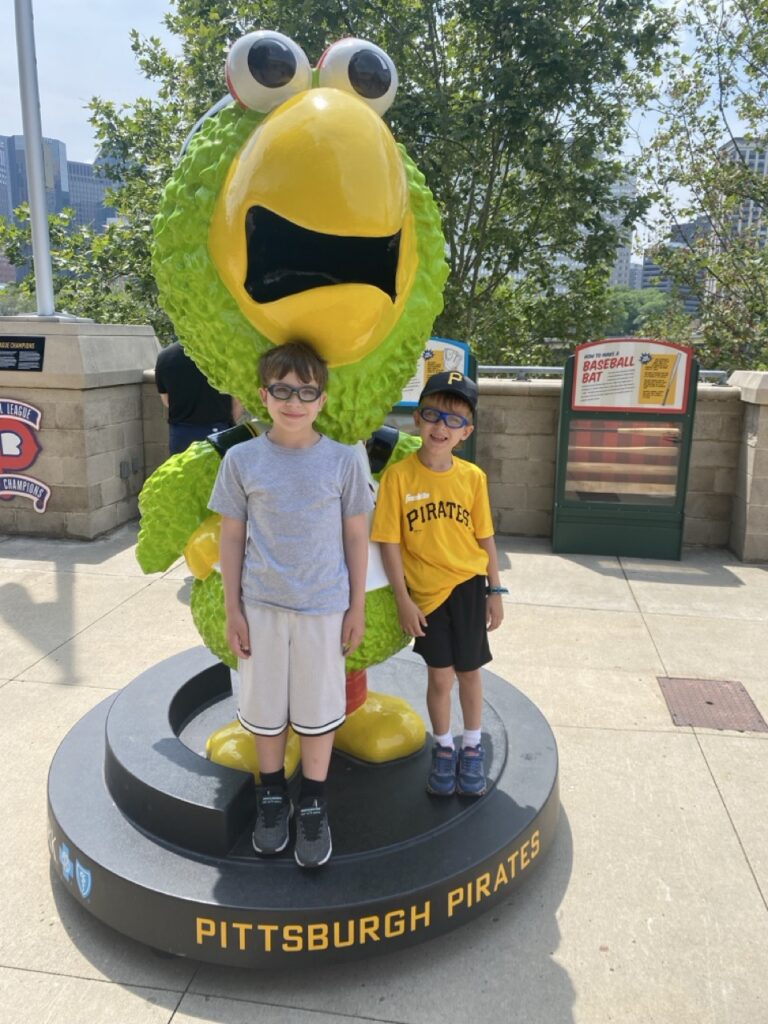Two boys stand with a Pittsburgh Pirates parrot statue.