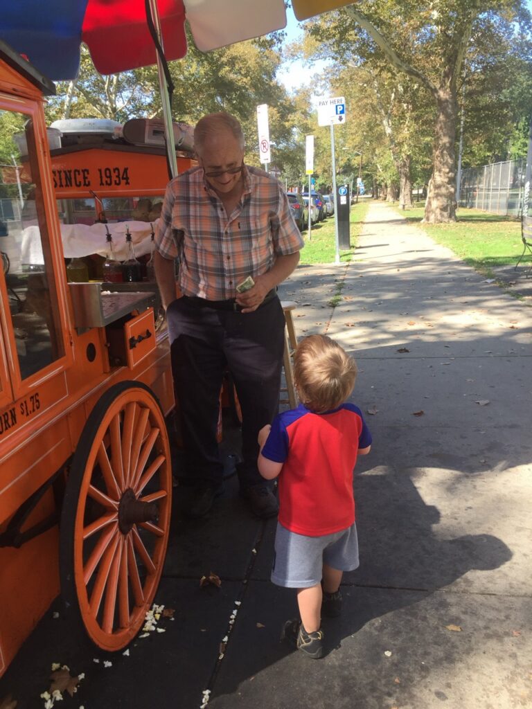 A little bus gives money to an older man running an ice treat stand.