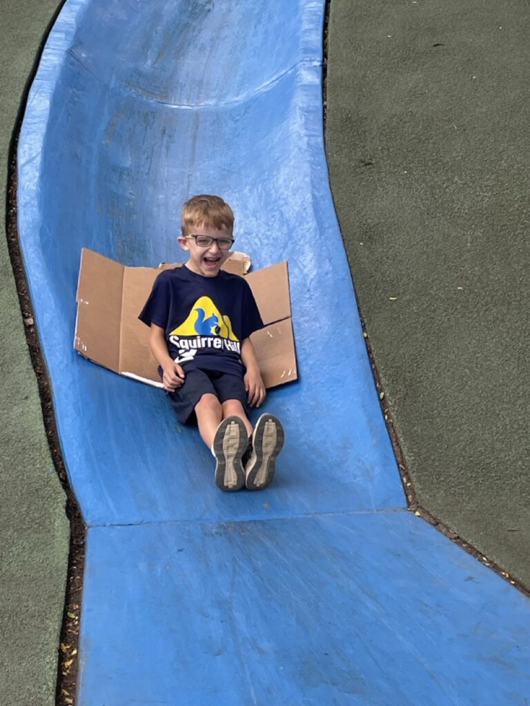 A boy slides down a blue slide on a piece of cardboard.