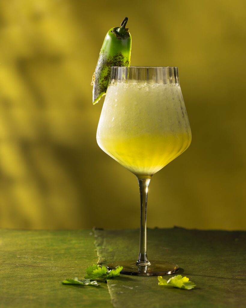 A tall stem wine glass with a frozen sauvignon blanc cocktail inside and a jalapeno pepper garnish with slices of jalapeno below the glass.