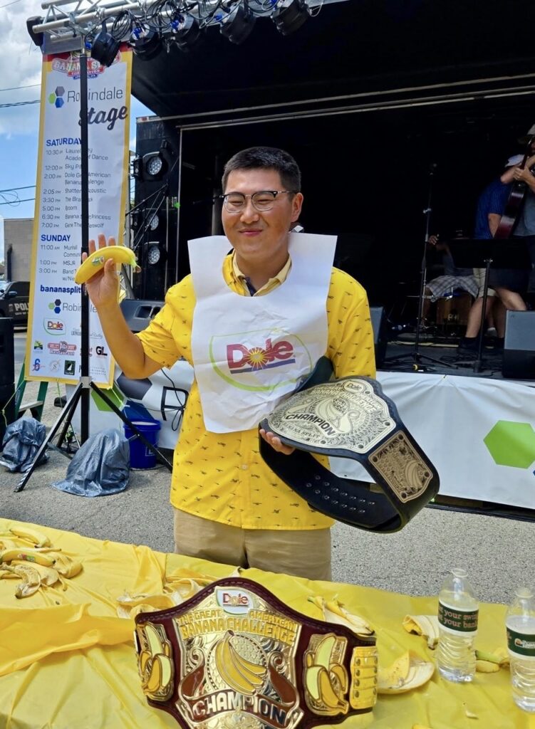 A man holds a banana with a dole white bib on and a championship belt in his other hand.