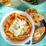 Spiced pickled peaches served in a bowl with white cheese and toasted baguette.
