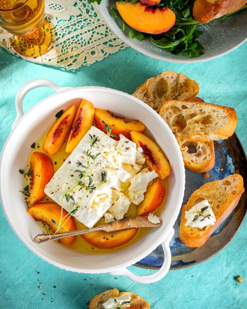 Spiced pickled peaches served in a bowl with white cheese and toasted baguette.