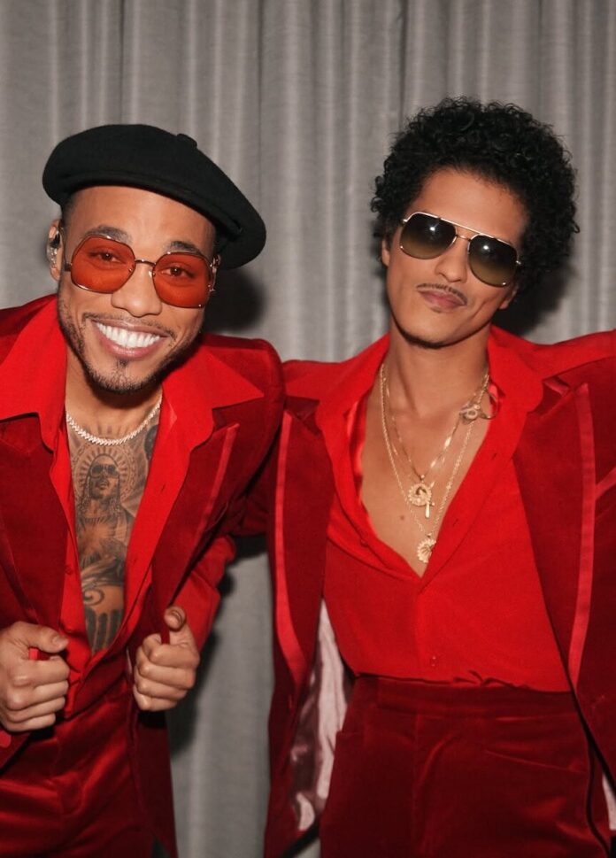 Bruno Mars and Anderson .Paak in red suits with sunglasses on in front of a silver curtain.