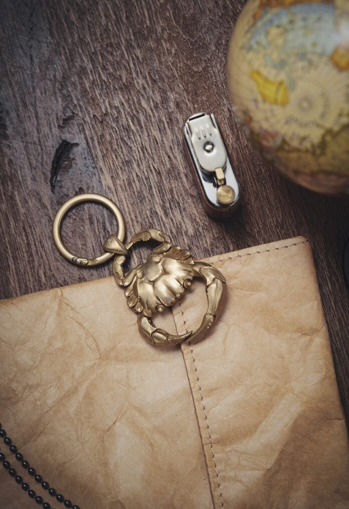 A gold crab keychain on top of a wood table and lather wallet beside a globe.