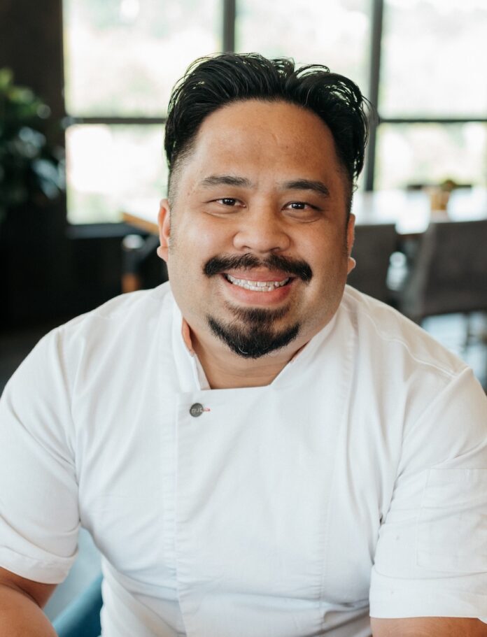 Chef Andrew Alvarez sits in a white shirt, smiling.