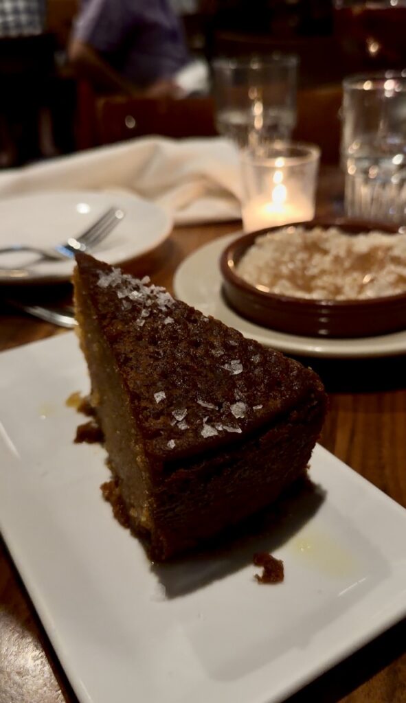 A plate of a slice of dark olive oil cake on a table.