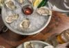 What’s Hot on Pittsburgh Menus This August? Local Food Influencers Reveal Their Recommendations Two steel plates of oysters on ice with sauce and lemon slices.