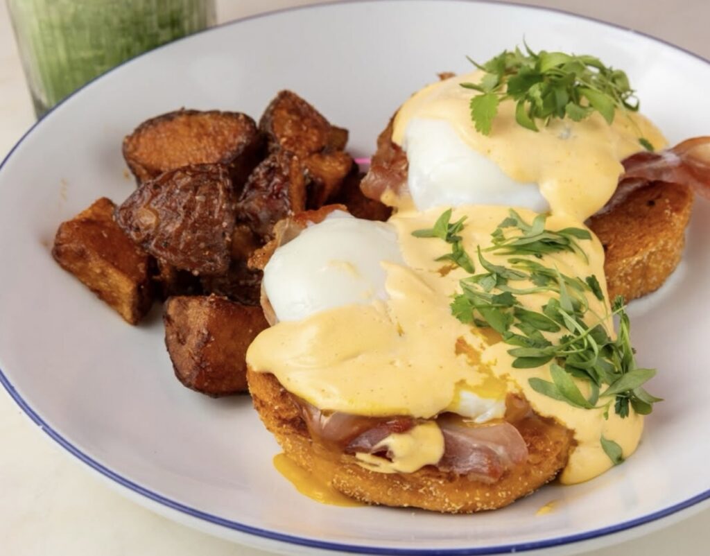 An eggs benedict with potatoes on the side of the plate.
