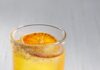 Golden Path Zero-Proof Recipe (Smoked Agave & Marigold Mocktail) An orange cocktail in a short glass with an orange slice inside all on a white table.