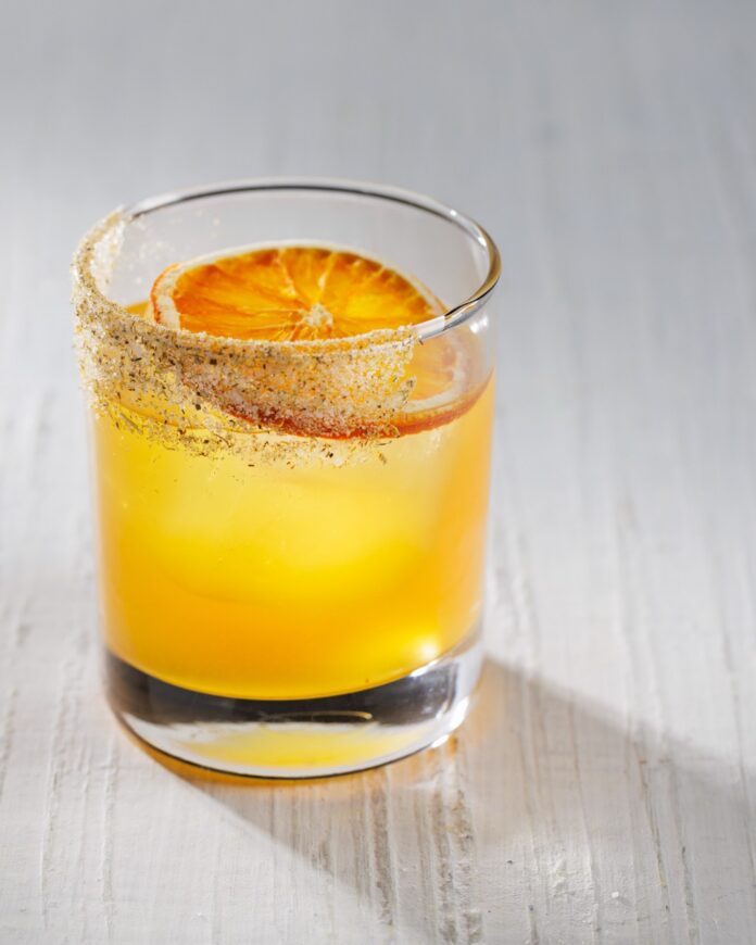 An orange cocktail in a short glass with an orange slice inside all on a white table.