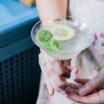 Woman holding a refreshing Grigio Spritz cocktail garnished with a lemon slice and fresh basil.