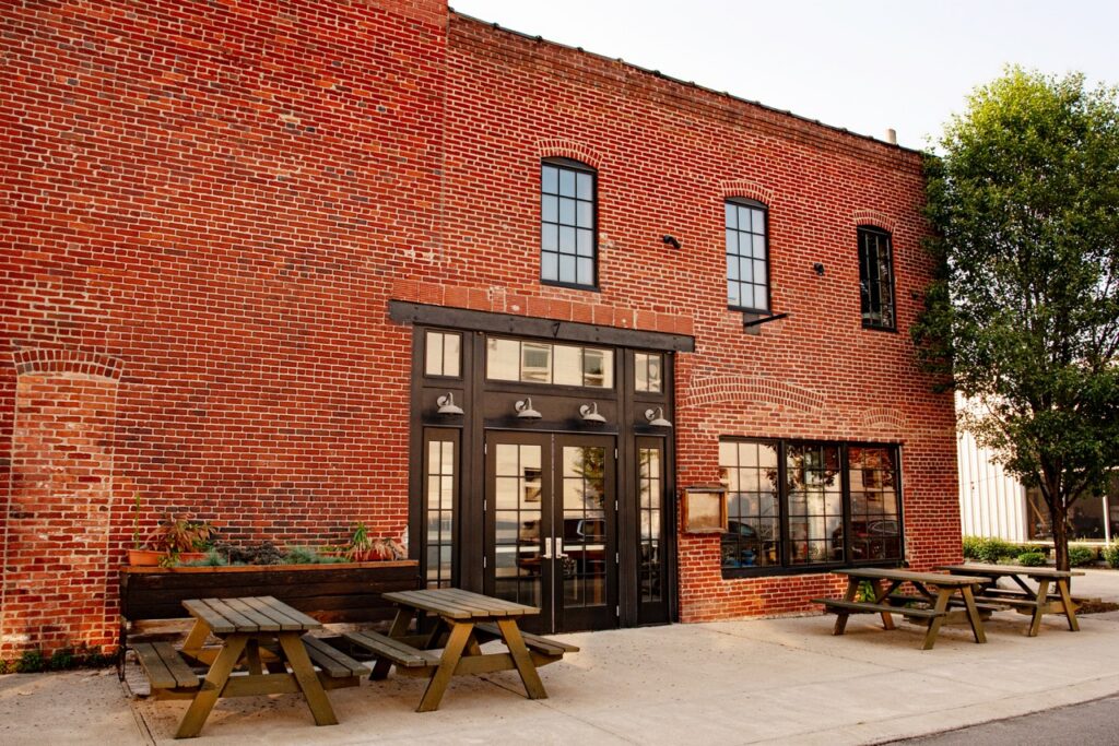 The outside of H. Obernauer and Co whiskey in the Strip district, a brick building with picnic tables outside.