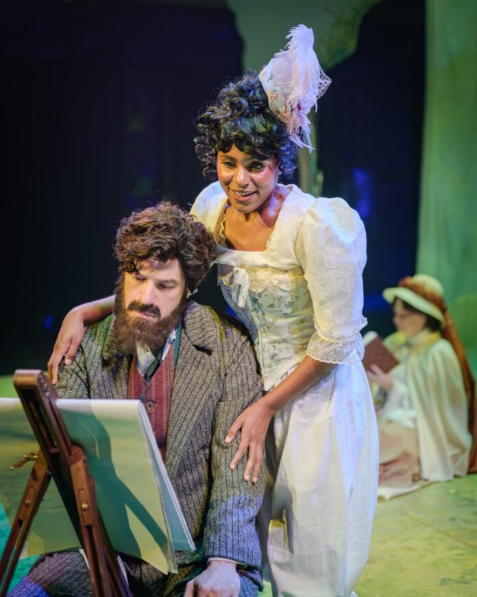 Live musical theater scene with a male actor sketching at an easel and a smiling actress in a white period dress.
