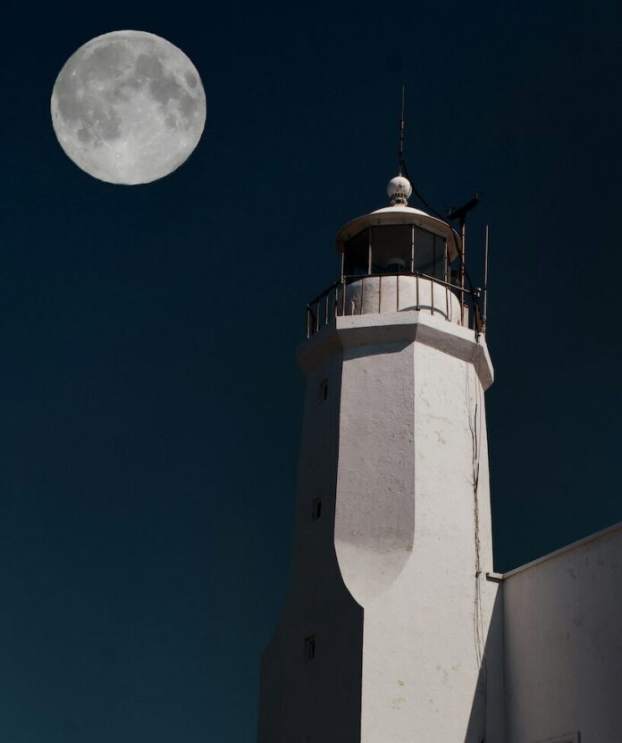 A full moon beside a tall white light house.