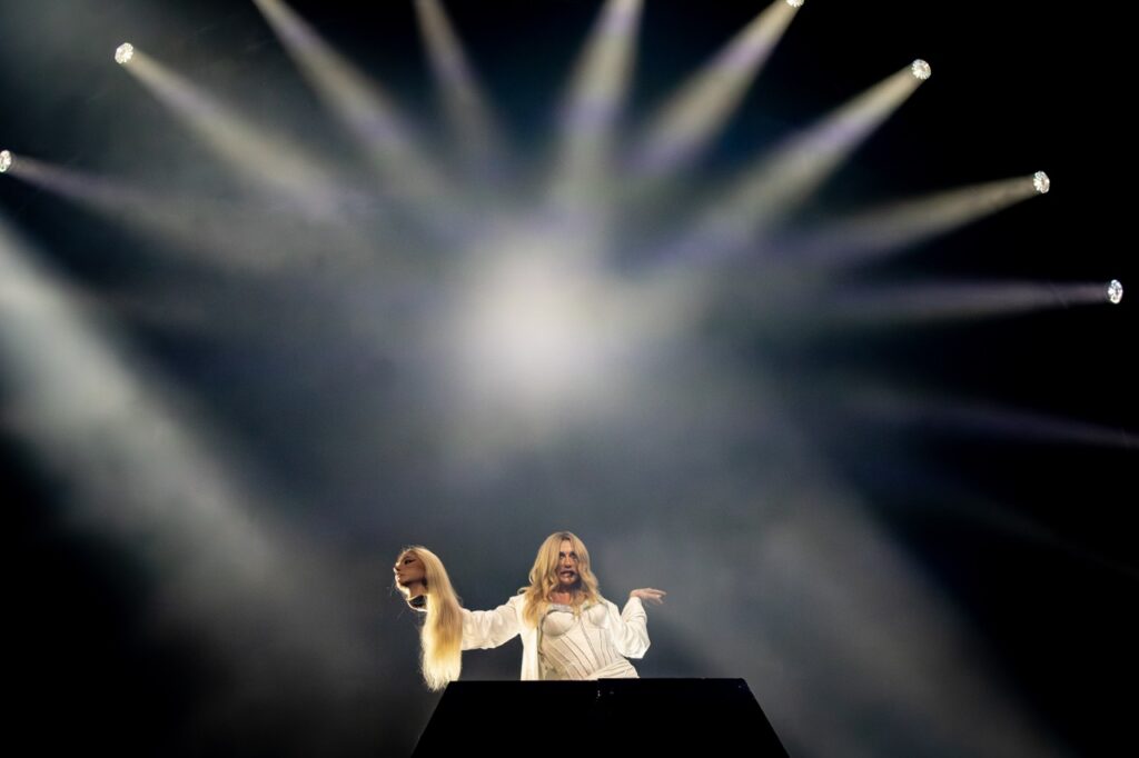 Kesha holding a mannequin head under lights on a stage.