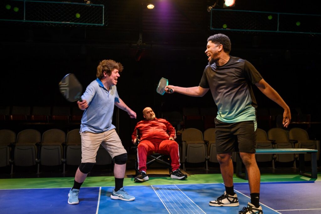 Two men playing pickleball on a stage, with an audience watching