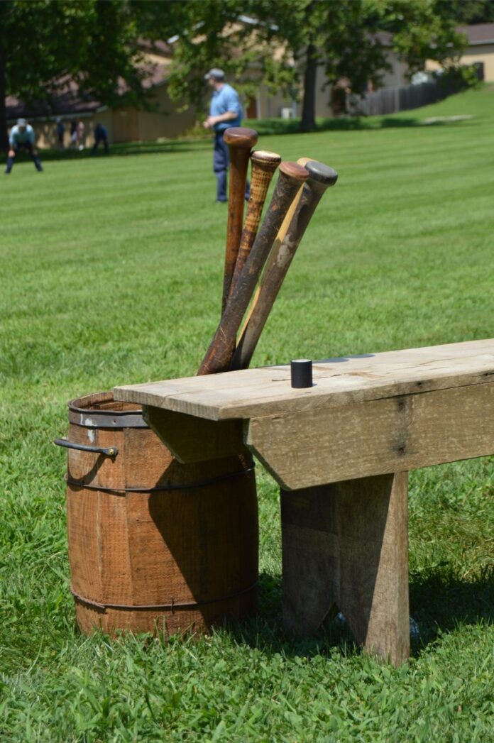 Vintage base ball bats lean against a bench in a bucket.