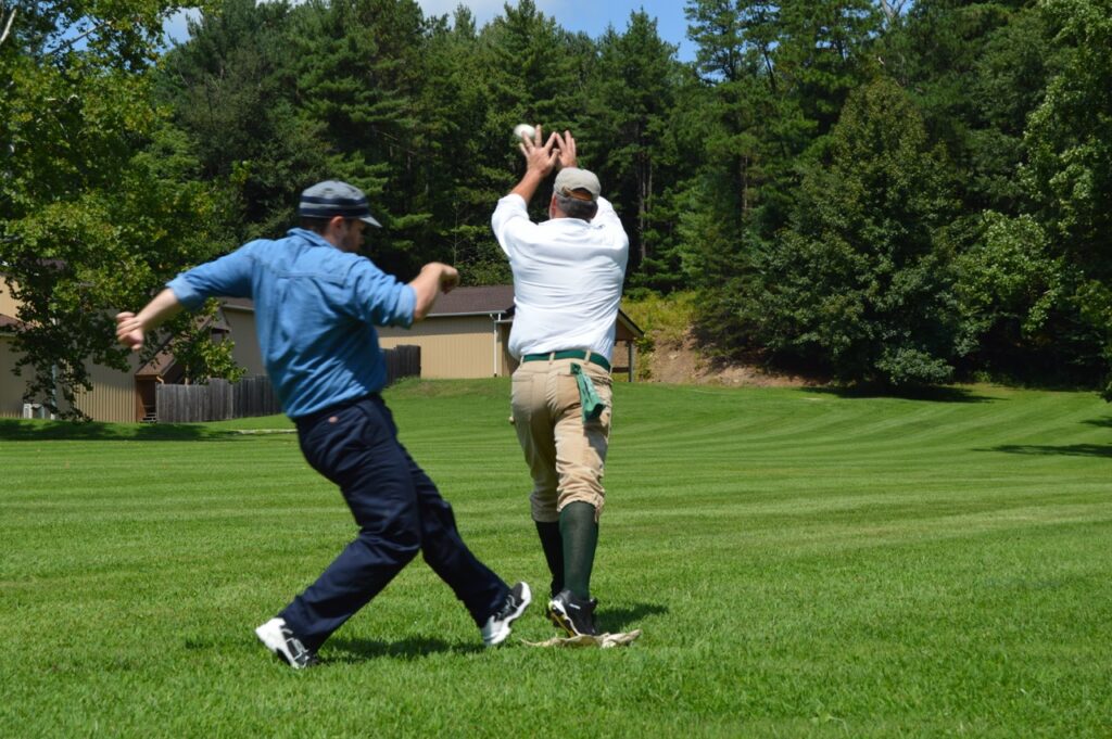 One player tries to run to a base while another holds his hands up to catch a ball.