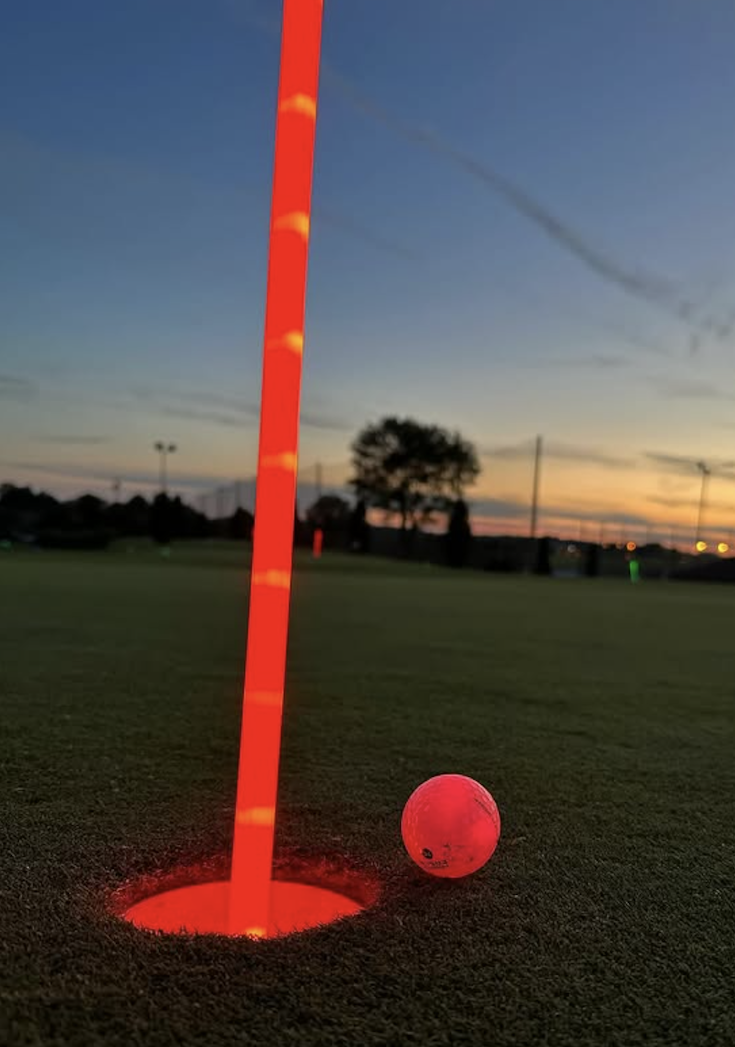 A glowing golf flag in a hole glowing red with a red golf ball beside it on the green. 