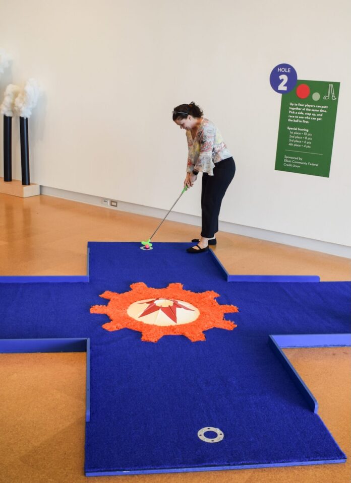 A woman plays on a blue mini golf course inside the Westmoreland Museum of American Art.