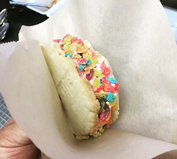 A person holding an ice cream sandwich rolled in fruity pebbles.