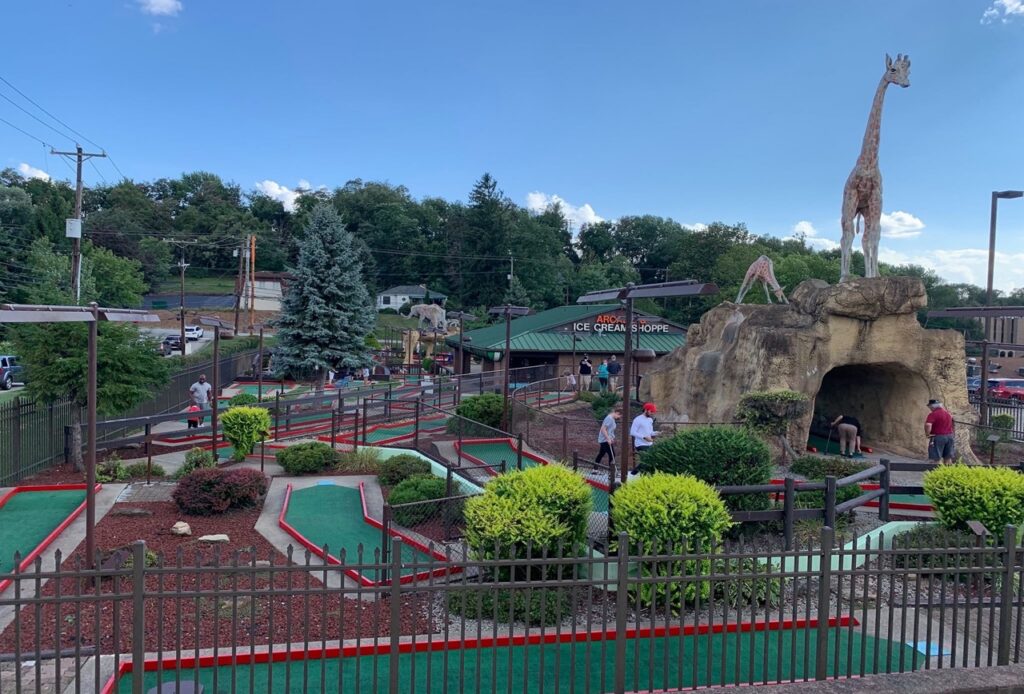 A mini golf course outside with greenery and a giraffe statue.