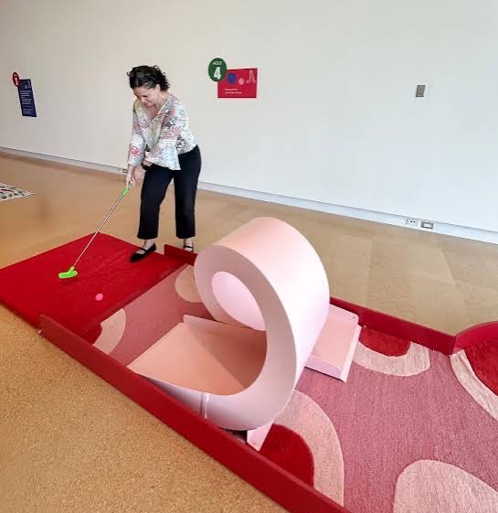 A person plays putt-putt inside the westmoreland museum on a pink and red course.