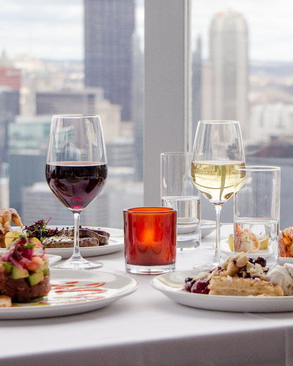 A table with food and wine in front of a window with a view of the city skyline in Pittsburgh.
