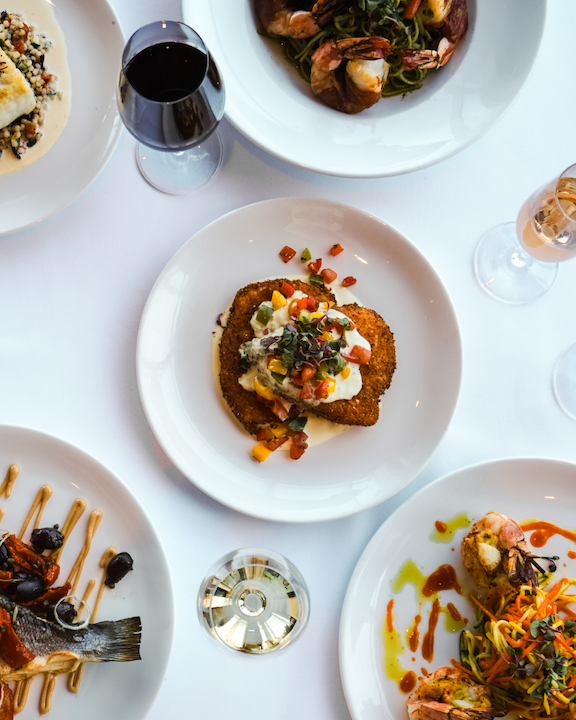 A downshift of several plates of food and glasses of wine.