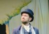 Nancy Zionts of Front Porch Theatricals Teaches Us How to Watch a Musical A man in a musical performance on stage in highbrow blue clothing with a cane and a hat, holding his pocketwatch in his hand.