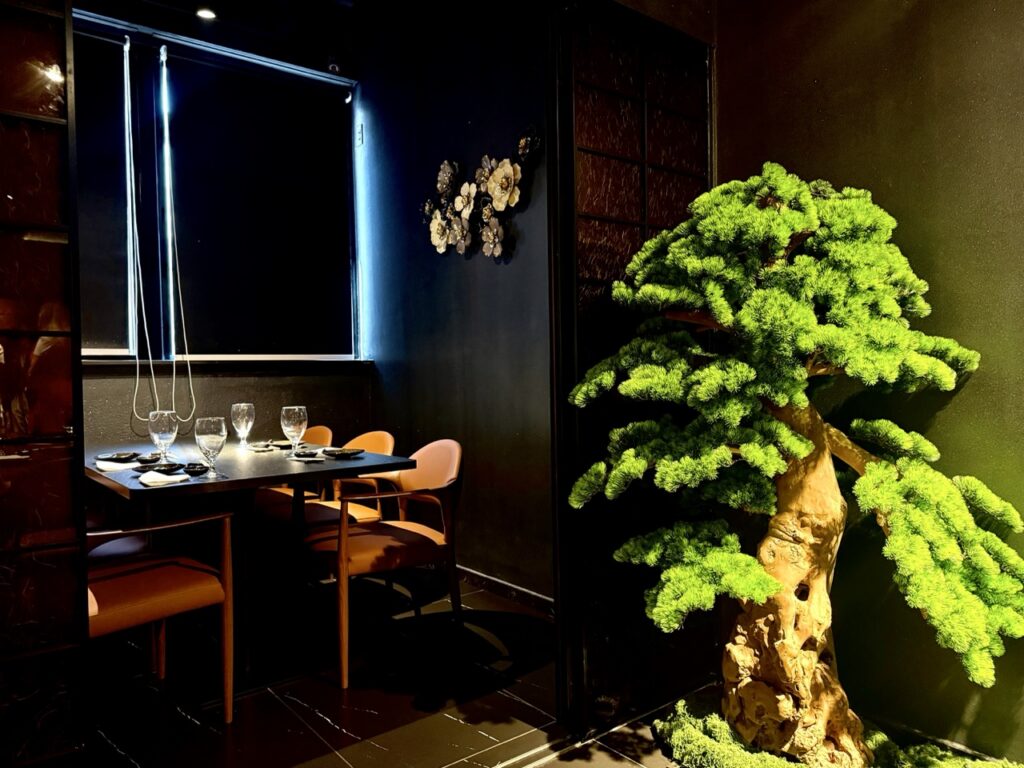 The inside of Okane dining room with a bonsai tree in the corner beside a table.