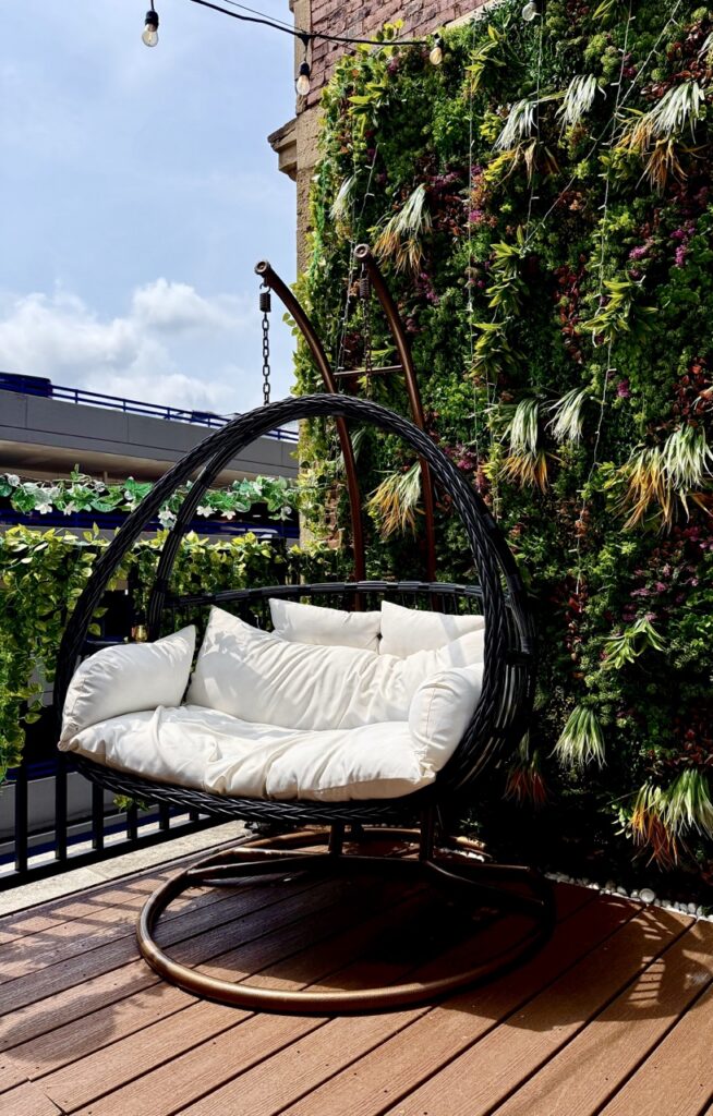 A swing on the rooftop in front of a floral green wall.