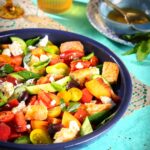 Peach and tomato pantoush salad with toasted bread, feta, and fresh herbs in a blue bowl.