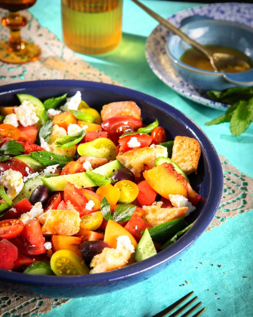 Peach and tomato pantoush salad with toasted bread, feta, and fresh herbs in a blue bowl.
