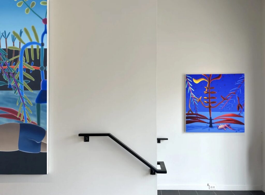 Two blue paintings of shapes and trees on a gallery wall.
