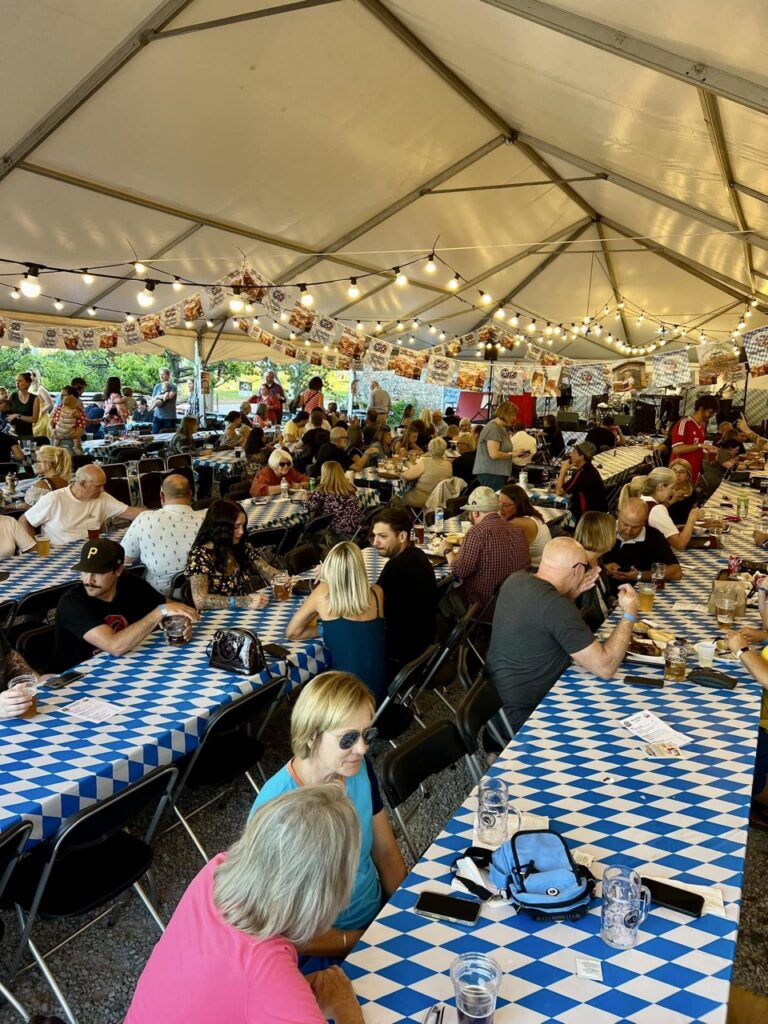 The inside of a tent with German table cloths and strung lights up above.