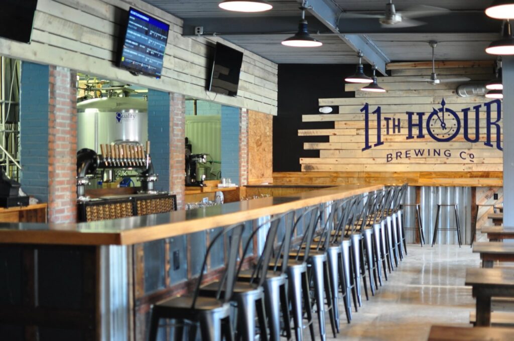 The inside of Eleventh Hour Brewing with chairs at a long wood bar.