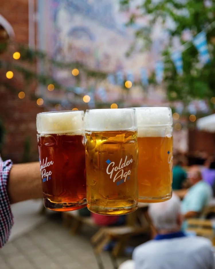 A person carrying three steins of beer outside.
