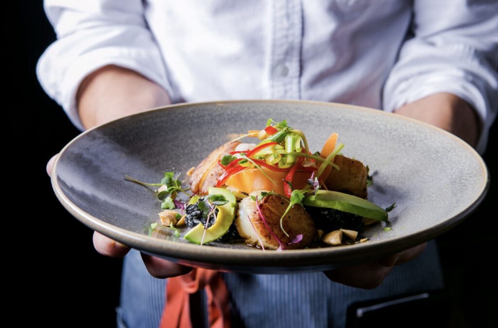 A person holds out a plate of seafood.