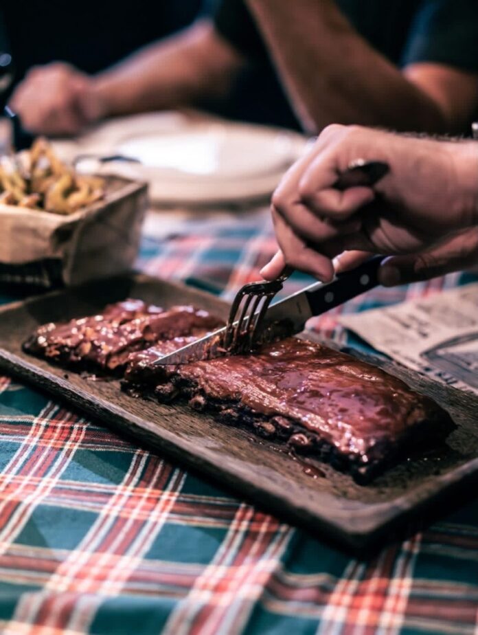 The Best Barbecue in Nice France at Bootgrill TABLE Magazine A rack of barbecue ribs being sliced on a wooden platter at Bootfire restaurant in Nice.