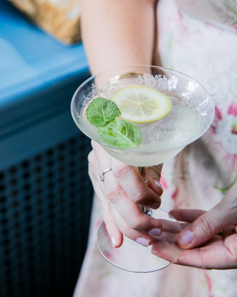 Close-up of a guest in a floral dress holding a refreshing pinot grigio spritzer at a summer Mah Jongg luncheon.