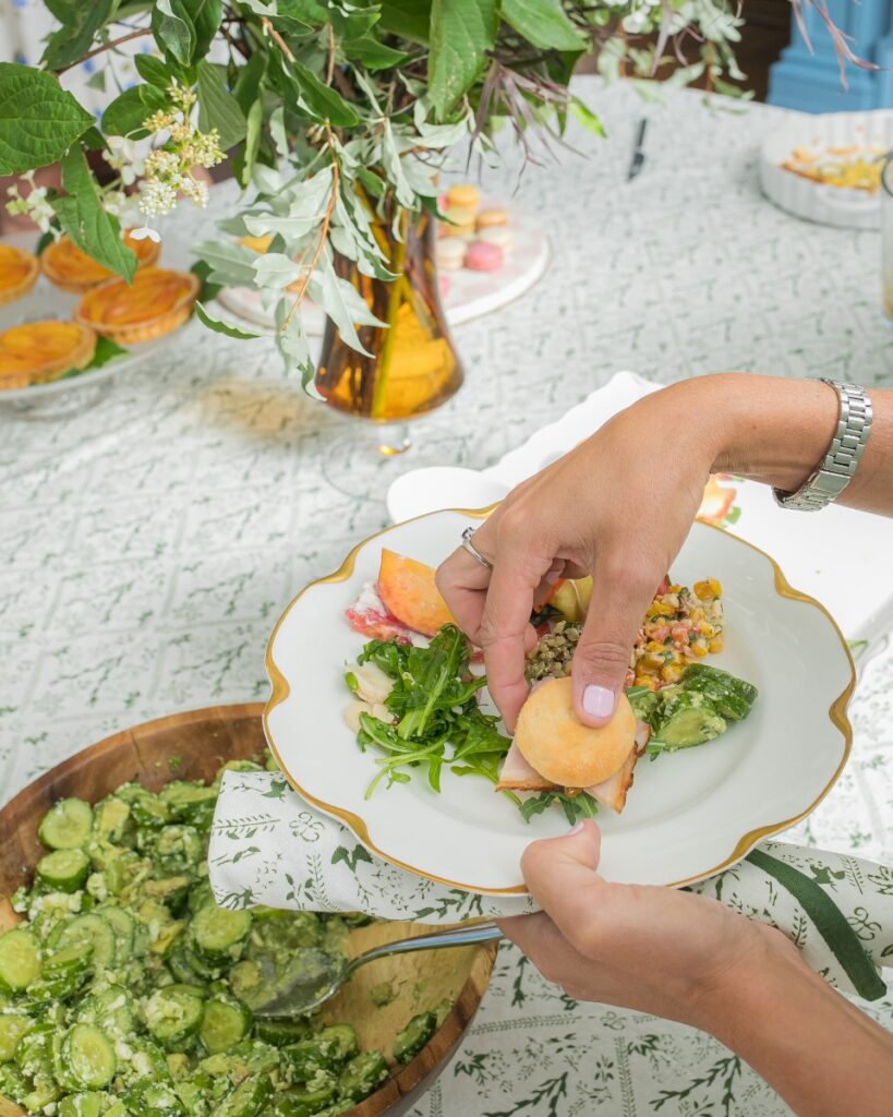 Close-up of a guest plating a ham biscuit and light summer salads at a Mah Jongg potluck.