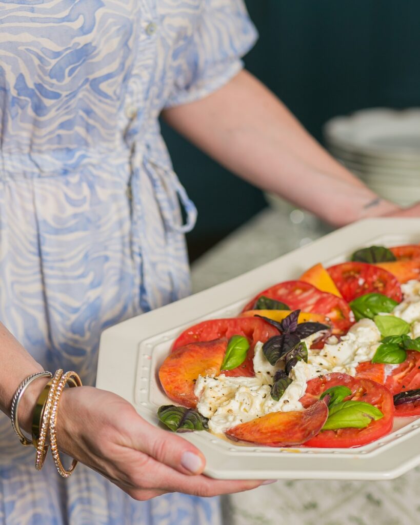 Guest holding a platter of fresh heirloom tomato and mozzarella salad for a summer Mah Jongg luncheon.