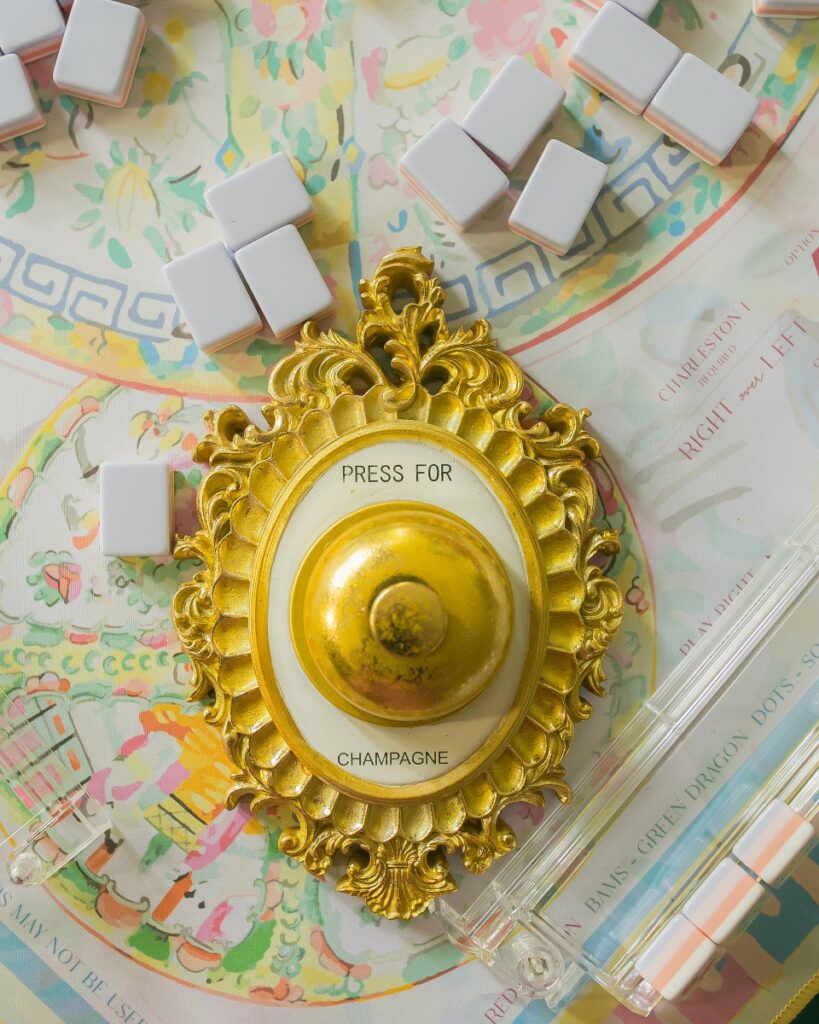 Pastel Mah Jongg tiles scattered around a vintage gold Press for Champagne button on a decorative play mat.